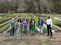 Board members and volunteers in front of a farms with rows of green crops