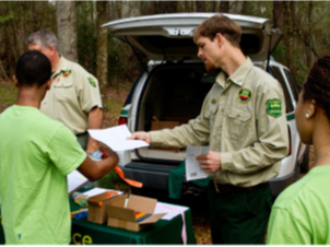 FL Forest Service ranger handing a paper to students in green shirts